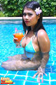 Holding glass seated in swimming pool wearing bikini